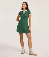 Vestido corto de mujer, estilo skater, color verde oscuro con cuello polo y ribetes blancos en el cuello, puños y hombros. Presenta un escote en V y mangas cortas.