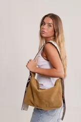 Bolso de hombro tipo hobo de gamuza color marrón óxido, con correa ancha ajustable de color negro y herrajes metálicos plateados. El nombre de la marca "GANESHA" está grabado sutilmente en el cuerpo del bolso.