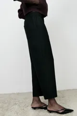 Pantalón de lino negro, de tiro alto, con bolsillos delanteros de vivo, pernera recta y cierre frontal con cremallera, botón interior y gancho metálico.