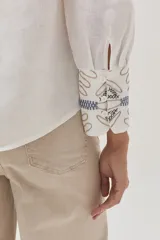 Camisa blanca de lino con bordados florales en tonos beige y azul.