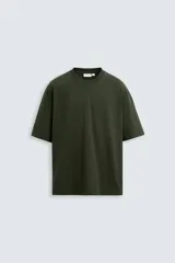 Camiseta verde oscuro de corte holgado, confeccionada en tejido de algodón grueso. Tiene cuello redondo y mangas cortas sin costura en la sisa.