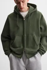 Sudadera negra relaxed fit de algodón compacto con interior en rizo, cuello con capucha ajustable, manga larga, bolsillos frontales tipo canguro, acabados en rib y cierre frontal con cremallera.