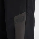 Pantalón deportivo New Balance para mujer, color negro con paneles laterales en gris oscuro. Presenta cintura elástica fruncida y puños ajustados en los tobillos.