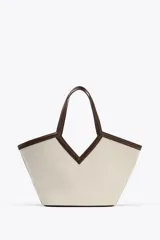 Bolso tipo shopper color crudo, con cuerpo de lona y detalles en cuero marrón. Tiene doble asa de hombro y una bolsa interior extraíble con cierre de cremallera. Se cierra con un lazo.