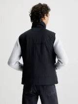 Chaleco negro acolchado de nailon reciclado con cuello alto, cierre de cremallera, bolsillos con cremallera en la cintura y logo de Calvin Klein en el pecho y la nuca.