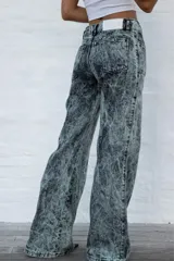 Jean de mujer de corte recto y tiro alto, con efecto acid wash en tonos gris y verde claro. Presenta costuras frontales y traseras que simulan pliegues, y etiqueta de marca blanca en la parte trasera de la cintura.