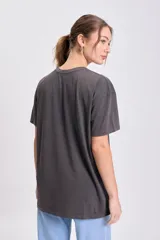 Remera oversize de manga corta, color gris oscuro con efecto gastado, con estampado frontal de Alicia en el País de las Maravillas, incluyendo el texto "ALICE In Wonderland" rodeado de flores.