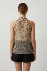 Top sin mangas de poliéster con estampado abstracto en tonos beige, marrón y dorado. Presenta cuello halter con abertura en la espalda y cierre con botones.
