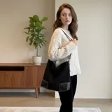 Bolso tipo hobo o tote de eco cuero con textura símil gamuza en color negro. Presenta detalles de pespuntes en color blanco en la base, que es de cuero liso negro. Tiene correa de hombro delgada y ajustable.