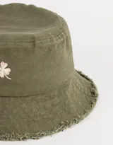 Piluso verde militar de denim con ala corta y bordado de un trébol de cuatro hojas en color rosa. El borde del ala está desflecado.