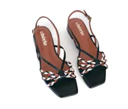 Sandalia de cuero negra con tiras finas y detalle frontal trenzado en colores blanco, marrón y negro. Pulsera ajustable con hebilla metálica y base plana con taco bajo geométrico.