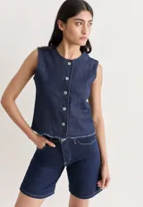 Chaleco sin mangas de denim azul oscuro, con cuello redondo y cierre frontal de botones plateados. El ruedo inferior tiene un acabado deshilachado.