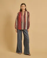 Blusa de algodón a rayas verticales rojas, marrones, azules y blancas, con cuello abierto, escote estrecho y mangas largas ligeramente abullonadas.