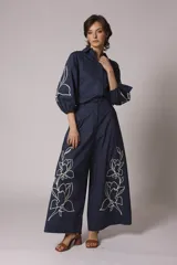 Pantalón palazzo azul marino con bordado de flores blancas en la parte inferior de ambas piernas. El pantalón tiene talle alto y pinzas en la cintura.