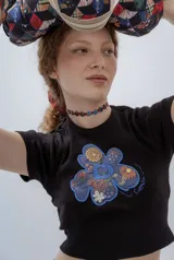 Remera negra de punto con cuello redondo y mangas cortas. Presenta un aplique de flor con estampado floral y borde azul en el frente.