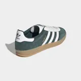 Championes Adidas Gazelle Indoor de color verde oscuro con las tres tiras laterales blancas y suela de goma color caramelo. Presentan un exterior de cuero con detalles sintéticos, cordones blancos y el nombre del modelo grabado en dorado.