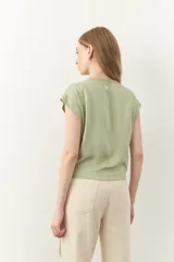 Blusa negra con escote en V cruzado, mangas cortas y detalle de encaje en la parte superior. Tiene un lazo en la cintura para ajustar.