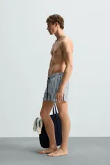 Bañador de hombre confeccionado en tejido técnico con textura. Diseño a rayas verticales en tonos azul y blanco. Cintura elástica ajustable con cordón. Bolsillos laterales y detalle de bolsillo trasero de solapa. Bajo con aberturas laterales. Forro interior.