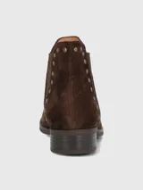 Botín de cuero color marrón oscuro con acabado de gamuza, diseño estilo Chelsea con paneles elásticos laterales y detalles de tachas doradas. Posee punta redonda, taco bajo de 3 cm y forro de algodón orgánico.