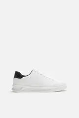 Zapatillas deportivas blancas con detalle de pieza a contraste en la parte posterior de color negro. Suela con volumen de diseño irregular.