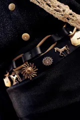 Cinturón negro de cuero con apliques de tachas plateadas y doradas con forma de soles, caballos y flores. Se ajusta con un lazo en la parte posterior.