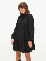 Vestido corto negro con cuello alto, mangas largas abullonadas y falda escalonada.