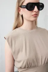 Top sin mangas color beige, confeccionado en tejido acanalado. Presenta hombreras definidas y un recorte fruncido bajo el busto que ajusta la silueta.