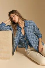 Camisa de manga larga, color azul, con cuello camisero y estampado geométrico en blanco. Presenta un diseño de doble capa: una camisa exterior abierta con botones y un top anudado debajo.