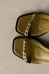 Sandalia de cuero color marrón con taco bloque medio y punta cuadrada. Presenta tachas esféricas doradas en las tiras y hebilla de ajuste en el tobillo.