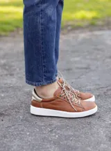 Zapatillas acordonadas de cuero color marrón con detalles dorados en el talón y suela blanca.