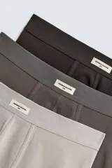Pack de tres calzoncillos tipo bóxer de tejido elástico con acabado aterciopelado y cintura elástica. Incluye un bóxer color gris claro, uno gris oscuro y uno marrón.
