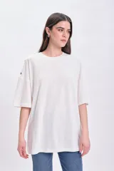 Remera blanca de corte holgado con cuello redondo y mangas cortas. Presenta detalle de ojales metálicos en los hombros.