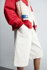 Bermuda de denim color blanco roto con efecto encerado, corte amplio (baggy fit) y cinco bolsillos. Presenta cierre frontal con cremallera y botón.