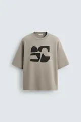 Camiseta color visón de corte relaxed fit, confeccionada en tejido interlock de algodón con elasticidad. Tiene cuello redondo, manga corta y estampado frontal con textura combinada a contraste en color negro.