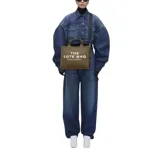 Tote bag de lona color beige con la inscripción "THE TOTE BAG MARC JACOBS" en el frente. Incluye cierre de cremallera, asas superiores y una correa de hombro ajustable y extraíble de color negro.