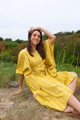 Vestido túnica amarillo con rayas verticales blancas, corte amplio, mangas cortas y lazo para ajustar en la cintura.