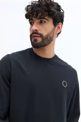Remera de manga larga color negro, con escote redondo y un pequeño logo circular estampado en el pecho.