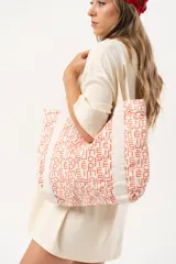 Bolso tipo tote bag de tela color crudo con estampado de letras en color naranja. Tiene asas de hombro de tela con diseño de espiga y un bolsillo frontal.
