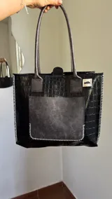Bolso tote negro con textura símil cuero de cocodrilo, bolsillo externo color beige y asas marrones.