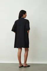 Camisa negra de manga corta, estilo kimono o bata ligera, con cuello solapa y bolsillos frontales amplios.