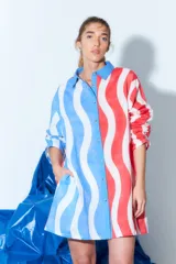 Túnica tipo vestido camisero corto con estampado de rayas onduladas verticales en colores rojo, blanco y azul. Tiene cuello camisero, cierre frontal con botones y mangas largas con puños abotonados.
