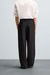 Pantalón negro de corte amplio con cinturón de tela con hebilla metálica. Presenta pliegues frontales, bolsillos laterales y traseros. Cierre frontal con cremallera y botón.
