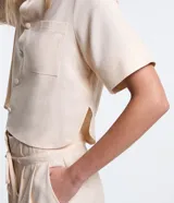 Camisa color beige claro, corta, con cuello inglés, manga corta, bolsillo en el pecho y abotonada adelante.
