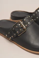 Sueco destalonado de cuero vacuno color negro, con hebilla ajustable dorada y detalles de tachas doradas.