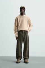 Sweater color beige con motas de colores, de tejido de punto grueso con cuello redondo y mangas largas. Presenta roturas y agujeros en el frente y las mangas.