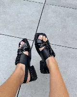 Sandalia negra de cuero con puntera cuadrada, tira ancha con nudo fruncido y tira fina ajustable en el talón. Posee un taco bajo y grueso.