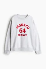 Buzo gris melange oversized con cuello redondo ribeteado acanalado y diseño de texto en rojo con la leyenda "Monaco 64 France". Modelo con hombros caídos y remate acanalado en puños y bajo. Interior cepillado suave.