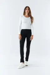 Pantalón negro de tiro alto, corte ajustado y aberturas en los tobillos.