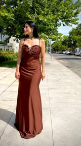 Vestido largo de fiesta color marrón chocolate, con breteles finos, escote fruncido y detalle de adorno metálico en el centro.