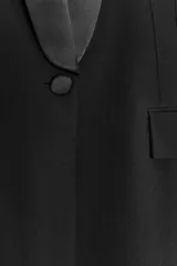 Blazer negra de corte clásico con cuello smoking de satén, manga larga con hombreras, bolsillos con solapa y cierre frontal con botón.
